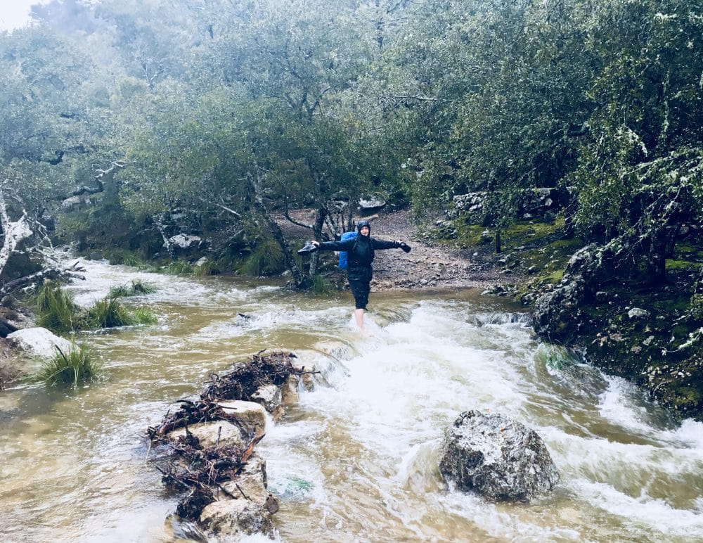 Wanderer balanciert auf überfluteter Steinbrücke auf dem GR 221