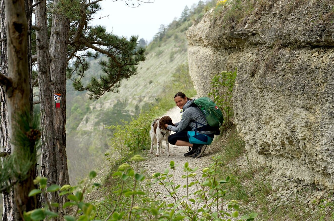 lächelnde Wanderin mit Hund auf schmalem Felsenweg